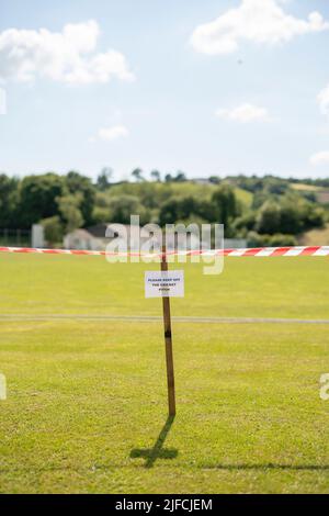 Un panneau indiquant « Please Keep off the cricket pitch » avec bande d'avertissement dans un village rural. Banque D'Images