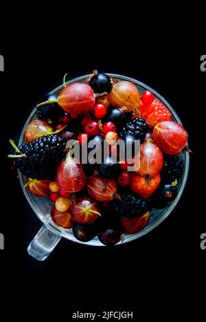 Baies de framboises, mûres, groseilles à maquereau et raisins de Corinthe dans une tasse sur fond noir. Banque D'Images