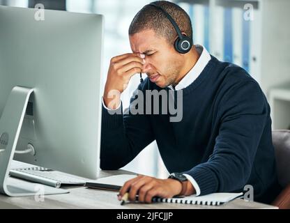 Un agent de centre d'appels homme stressé se fait mal de tête lorsqu'il travaille sur un ordinateur au bureau. Conseiller mixte de course faisant des erreurs et de la difficulté avec Banque D'Images