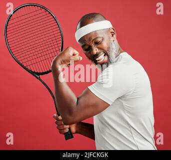 Un heureux africain américain mature debout sur fond rouge en studio, en flexion de son biceps tout en posant avec une raquette de tennis. Noir souriant Banque D'Images