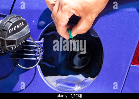 Image de la main d'un homme qui avec un compte-gouttes met de l'essence au réservoir de la voiture. Référence à l'augmentation constante des prix du carburant Banque D'Images