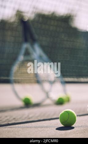 Groupe de balles de tennis et de raquettes contre un filet sur un terrain vide dans un club sportif pendant la journée. Jouer au tennis, c'est faire de l'exercice, favorise la santé Banque D'Images
