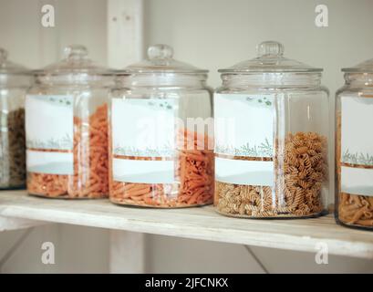 Pots en verre de différents types de pâtes alignés sur une étagère de présentation dans une épicerie. Rendez-vous au épicier local pour tous vos besoins culinaires Banque D'Images
