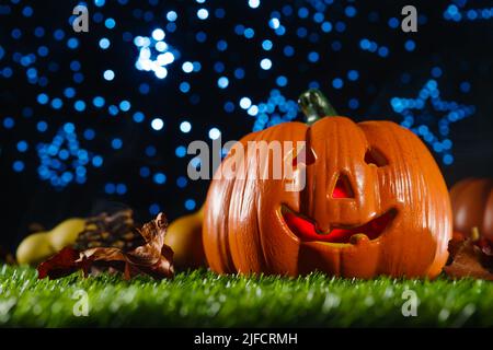 Une citrouille d'Halloween orange avec un visage sculpté illuminé de l'intérieur par une bougie sur l'herbe verte contre un ciel étoilé bleu. Bannière, affiche, inlit Banque D'Images