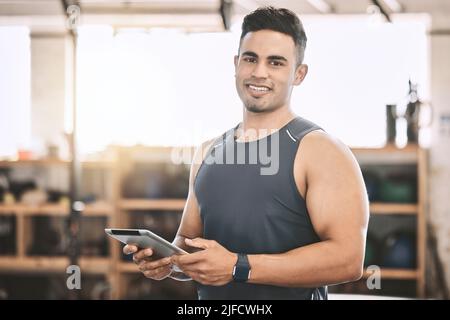 Entraînez-vous avec un entraîneur de gym en effectuant un programme d'entraînement sur une tablette. Un entraîneur puissant et musclé utilisant une tablette numérique. Jeune bodybuilder utilisant un appareil sans fil Banque D'Images