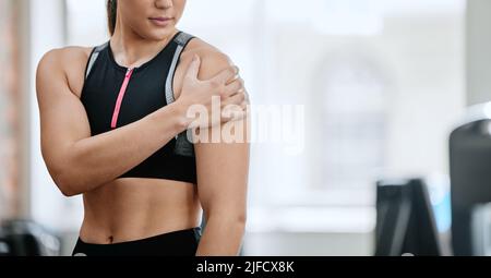 Entraîneur inconnu seul dans la salle de gym et souffrant de blessures d'épaule. Un entraîneur debout et bras de frottement pendant l'entraînement dans le club de santé d'exercice. Une femme Banque D'Images