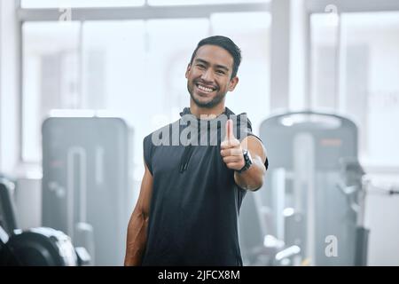 Portrait de l'entraîneur souriant seul dans la salle de gym, montrant le signe et le symbole du pouce levé. Entraîneur asiatique endossant le soutien après l'entraînement dans le club de santé d'exercice Banque D'Images