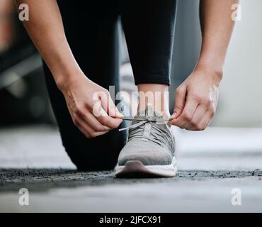 Gros plan d'un entraîneur inconnu qui noue des lacets seuls dans la salle de sport. Un entraîneur caucasien à genoux, se préparer à l'entraînement club de santé. Une femme qui s'est accroupie Banque D'Images