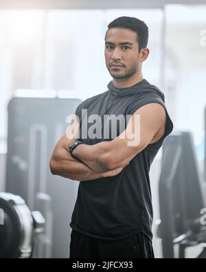 Portrait d'un entraîneur asiatique sérieux seul dans la salle de gym. Beau coach concentré debout avec les bras croisés après l'entraînement dans le club de santé. Jeune confiant Banque D'Images