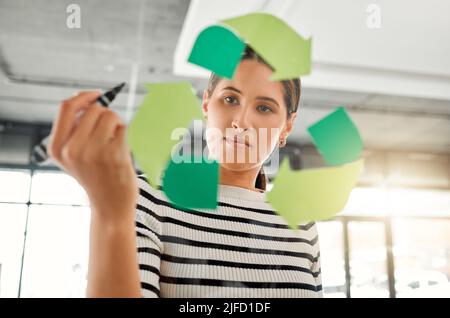 Jeune femme d'affaires de course mixte ciblée dessinant un symbole de recyclage sur une fenêtre en verre dans un bureau au travail. Un homme d'affaires hispanique sérieux qui dessine un Banque D'Images