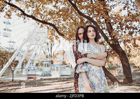 Deux jeunes femmes vêtues de robes vintage s'embrassent à l'automne stationnement Banque D'Images