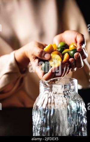 Remplissage du pot de boisson avec des kumquats et de petites limes, frais et fruité de boisson froide processus de fabrication - photo de stock Banque D'Images