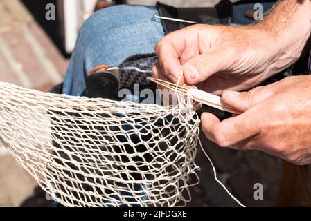 Enkhuizen, pays-Bas. Juin 2022. Les mains d'un pêcheur réparant des filets de pêche avec des aiguilles et des fils. Photo de haute qualité. Gros plan. Banque D'Images