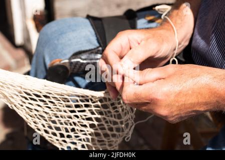 Enkhuizen, pays-Bas. Juin 2022. Les mains d'un pêcheur réparant des filets de pêche avec des aiguilles et des fils. Photo de haute qualité. Gros plan. Banque D'Images