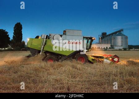 RÉGION DE TERNOPIL, UKRAINE - 03 août 2021: - Combiner le travail CLAAS de nuit dans le champ de blé près des réservoirs de stockage de grain, la récolte Banque D'Images