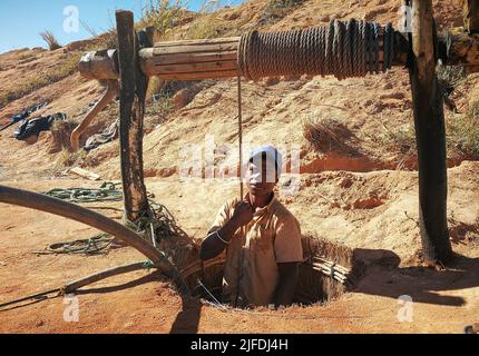 Ilakaka, Madagascar - 30 avril 2019: Inconnu homme malgache debout dans le sol mine de pierre précieuse trou ou puits, moitié corps visible, corde de maintien - abou Banque D'Images