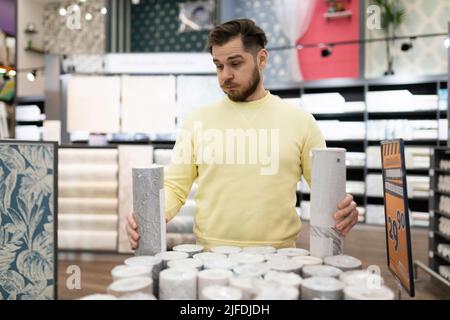 un homme dans un hypermarché de construction choisit papier peint pour coller de mur Banque D'Images