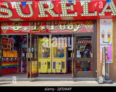 Une salle de jeux avec une machine de jeu d'un côté et deux machines avec jouets moelleux au centre. Une affiche de crème glacée se trouve sur un mur. Banque D'Images