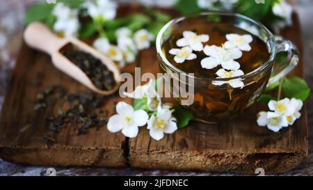 thé vert jasmin dans une tasse. Fleurs de jasmin, thé sec sur une surface en bois. Banque D'Images