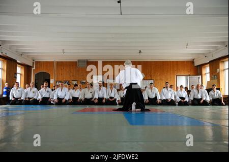 Groupe de stagiaires en kimono s'agenouillant sur le tatami à l'écoute de l'instructeur d'aikido avant de s'entraîner dans un club sportif. 6 février 2018. Kiev, Ukraine Banque D'Images