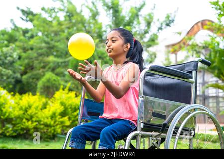 Concept de bonheur, de liberté et de plaisir en souriant seule fille enfant avec handicap jouant avec le ballon pendant que le fauteuil roulant au parc. Banque D'Images