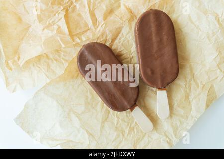 La glace au chocolat sur un bâton repose sur du parchemin recouvert de chocolat, de glace chaude, froide et délicieuse. Repos d'été. Vue de dessus Banque D'Images