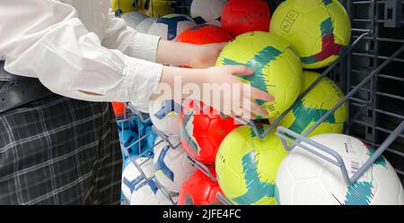 Moscou, Russie, Mars 2022: Quelqu'un choisit le ballon de sport parmi les boules multicolores de couleur blanc, jaune et rouge dans le magasin de sport Decathlon. Banque D'Images