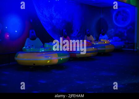 Voitures rondes à batterie tamponneuses dans une pièce sombre avec lumières clignotantes. Parc d'attractions. Attraction de fête pour enfants. Thème de l'OVNI et de l'espace. Banque D'Images