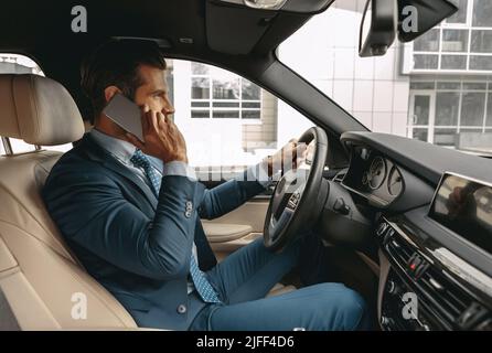 Taille vers le haut vue latérale portrait d'un homme caucasien beau ayant un voyage d'affaires en voiture tout en parlant sur un téléphone cellulaire Banque D'Images