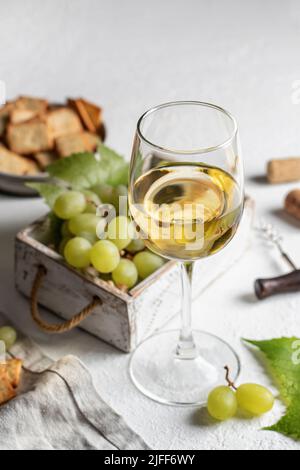 Verre de vin blanc avec raisins, corks et tire-bouchon et craquelins sur fond de table blanc Banque D'Images