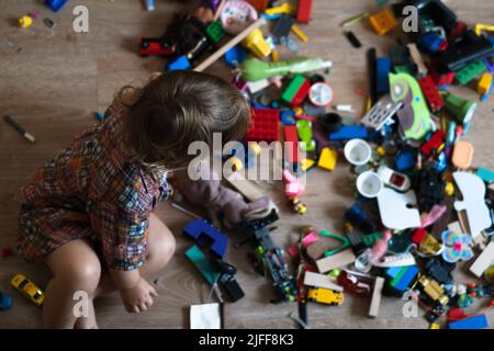 Mess dans la pépinière.Baby joue tout en étant assis sur le sol dans des blocs colorés. Concept de homeschooling Banque D'Images