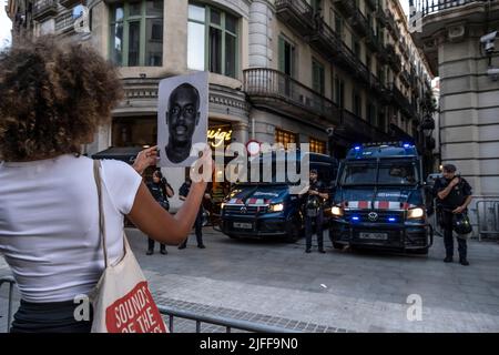 Barcelone, Espagne. 01st juillet 2022. Un manifestant tient un portrait d'Osamuyi Akpitaye, décédé en 2007 alors qu'il était déporté au Nigeria sur un vol Iberia, devant des policiers stationnés au poste de police de via Lietana. Des centaines de personnes ont manifesté dans le centre de Barcelone et ont finalement formé un autel sur la place Idrissa Diallo à l'occasion du massacre de Melilla où plus d'une trentaine de migrants africains sont morts en raison de la répression de la police marocaine après avoir essayé de sauter la barrière espagnole. (Photo par Paco Freire/SOPA Images/Sipa USA) crédit: SIPA USA/Alay Live News Banque D'Images