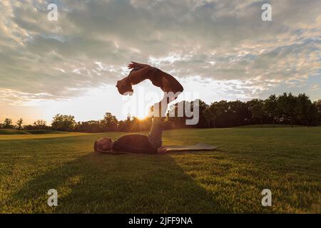 Un jeune couple fait de l'acro yoga dans le parc. Homme allongé sur l'herbe et femme d'équilibrage dans ses pieds Banque D'Images