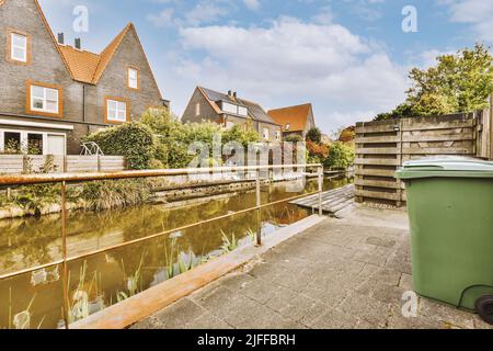 Vue sur des maisons grises de deux étages, des fenêtres à cadre blanc, des toits carrelés et un chenal d'eau, avec un réservoir vert sur la rive. Banque D'Images