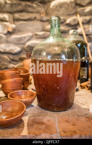 Vin jeune dans une grande bouteille de verre à côté d'une carafe en terre cuite géorgienne d'époque dans une authentique cave à vin géorgienne. Banque D'Images