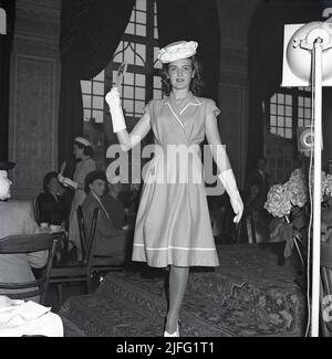 La mode des femmes en 1940s. Une jeune femme tenue en 1946. Une robe à la bonne longueur, chapeau et gants assortis. Le défilé de mode de la mode féminine de cette année se poursuit devant les gens dans un public. Suède 1946 Kristoffersson T148-5 Banque D'Images