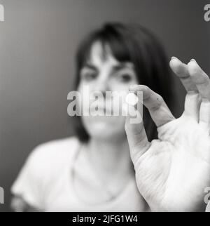 Dans le 1970s. Une femme hors foyer tient une pilule blanche entre ses doigts. Illustration de l'utilisation de médicaments ou de pilules contraceptives à l'époque. Suède 1971 Banque D'Images