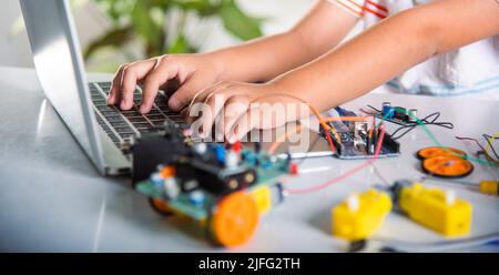 Un jeune garçon asiatique apprend le codage et la programmation avec un ordinateur portable pour la voiture robot Arduino, les jeunes élèves tapant le code dans l'ordinateur en ligne avec le jouet de voiture, STEA Banque D'Images