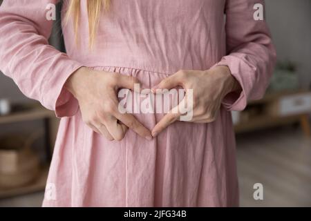 La femme enceinte fait la forme du cœur avec les doigts sur le ventre, gros plan Banque D'Images