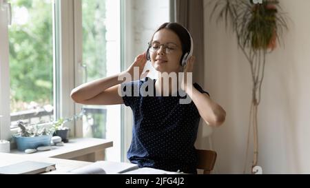 Une jeune fille étudiante paisible dans un casque sans fil qui écoute de la musique Banque D'Images