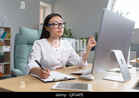 Jeune belle femme asiatique médecin travaille à distance à l'ordinateur dans le bureau de la clinique moderne, infirmière au travail papier avec l'ordinateur. Banque D'Images