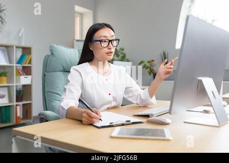 Jeune belle femme asiatique médecin travaille à distance à l'ordinateur dans le bureau de la clinique moderne, infirmière au travail papier avec l'ordinateur. Banque D'Images
