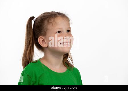 Une petite fille souriante dans un t-shirt vert regarde à droite, sur un fond blanc. Banque D'Images