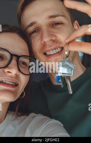 Portrait de tête de prise de vue joyeuse millénaire couple marié montrant des clés, heureux épouse et mari, propriétaires ou locataires faisant le selfie, acheté premier dwel Banque D'Images