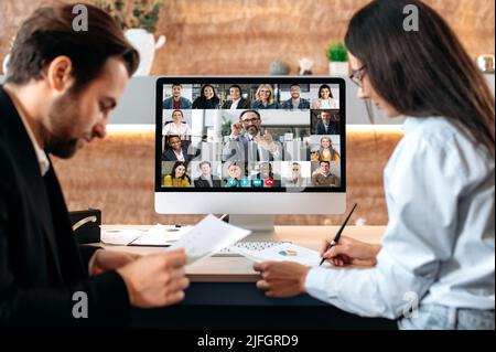 Travail d'équipe, concept de coopération. Des collègues du Caucase, un homme et une femme, parlant sur une vidéo conférence avec des employés multiraciaux, utilisant l'application et l'ordinateur, discutant de la dynamique de la croissance financière Banque D'Images