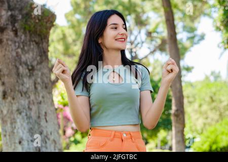 Jeune femme souriante confiante portant un t-shirt turquoise et un short orange sur le parc de la ville, à l'extérieur heureux et excité faisant le geste gagnant avec les bras levés, s Banque D'Images