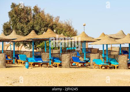 Plage de sable de la mer Rouge avec un groupe de parasols en paille et des chaises longues près de Marsa Alam, Egypte, Afrique. Banque D'Images