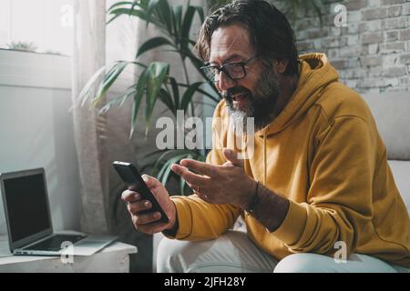 Homme à la maison dans la connexion d'appel vidéo activité de loisir à l'aide du téléphone. PC portable en arrière-plan. Les personnes qui font des activités de loisirs en intérieur utilisent la technologie et Internet Banque D'Images