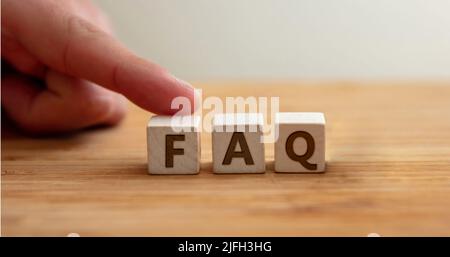 Concept FAQ. Le mot FAQ sur cube en bois avec le doigt pour montre la lettre F. Foire aux questions, message d'assistance, assistance, informations, réponse, Banque D'Images