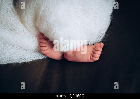 Jambes d'un nouveau-né. Pieds de bébé recouverts d'une couverture blanche. Le pied minuscule d'un nouveau-né en foyer doux sélectif. Photo de haute qualité Banque D'Images